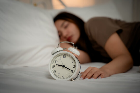 Insomnia concept of a young woman using a smartphone while lying awake in bed at night beside an alarm clock, showing sleeplessness, insomnia, smartphone, bedtime, sleep, fatigue	