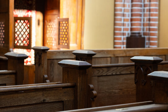 Traditional wooden church pews and carved wooden confessional booth illuminated by warm sunlight, historic church interior with brick wall