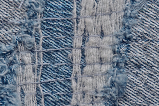 Macro photo torn blue denim fabric revealing vertical and horizontal thread details.