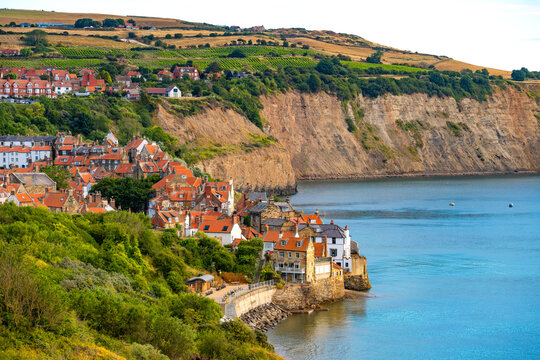 Early morning view of Robin Hood&rsquo;s Bay, with the historic fishing village, green cliffs and calm North Sea illuminated by warm summer sunlight in North Yorkshire, England.