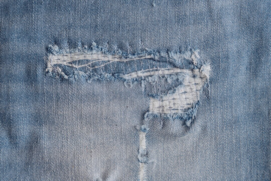 Close up distressed light blue denim jeans with large torn areas and white horizontal threads pattern.
