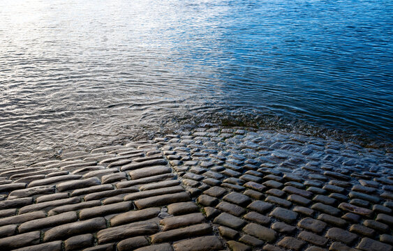 Old stone-paved slipway disappearing beneath the calm seawater at Robin Hood&rsquo;s Bay on the North Yorkshire coast, creating a strong pattern of stones, ripples and reflections.