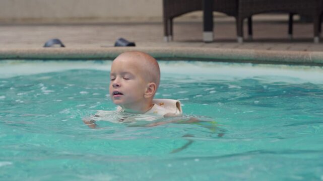 A carefree little boy swims peacefully with his eyes closed in a bright blue pool. He feels the refreshing water, enjoying a blissful moment during a fun summer day.