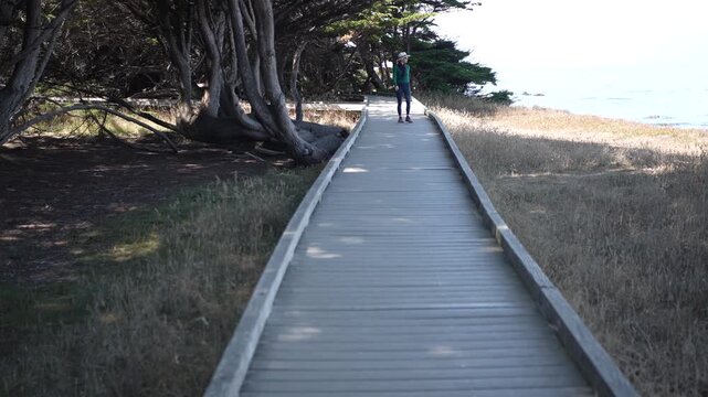 A senior woman enjoys a walk on the boardwalk at Mac Kerricher State Park in Fort Bragg, California next to the ocean on a clear day.