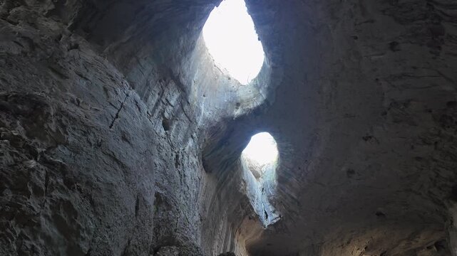 Majestic view looking up at the Eyes of God, two large, eye shaped holes in the ceiling of Prohodna Cave, Bulgaria. Sunlight streams through the openings