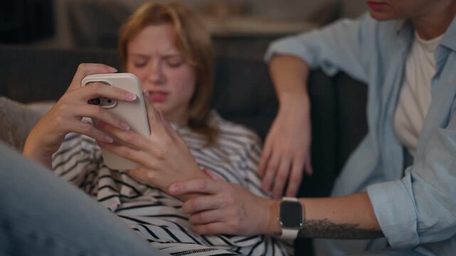 Close-up of teenage girl absorbed in smartphone while concerned mother tries to talk, illustrating teenage rebellion, screen time, digital distraction, family conflict and communication problems