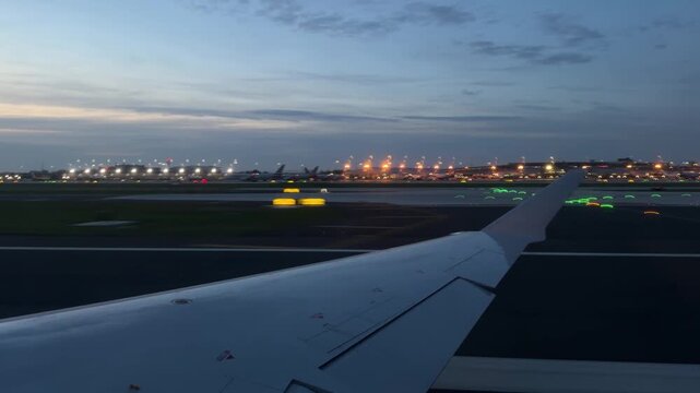 Airplane Wing View Through Window Of Passenger Seat at Sunset. Plane Takes Off From Airport into Sky. Blue Night Sky, Travel and Transportation