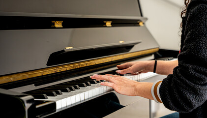 Woman playing black upright piano, learning music instrument © Fabian Vargas