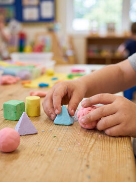 Toddler hands molding colorful playdough clay shapes at table