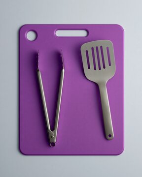 Purple Cutting Board with Stainless Steel Tongs and Spatula on Light Gray Surface