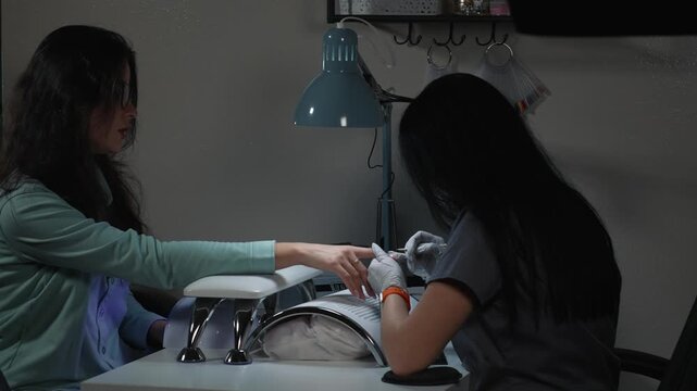 Applying and leveling polygel on nail plate with orange stick during salon nail extension procedure