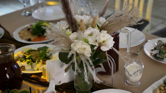 Festive table setting decorated with a bouquet of white eustoma flowers and pampas grass at a wedding or banquet