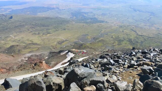 High camp on Mount Ararat seen in wide view from higher altitude, with rocky volcanic slopes and snowfields below, showing expedition scale, route elevation, summit approach, and mountain logistics