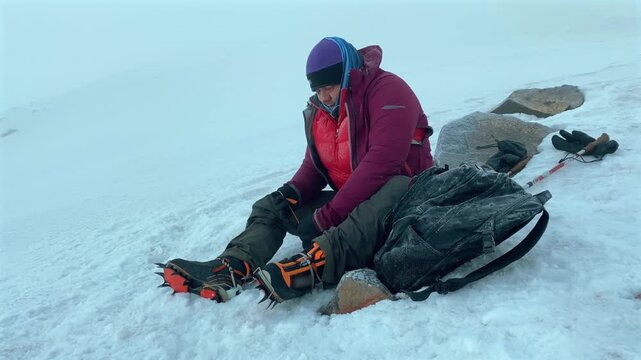 Mountaineer fastening crampons close-up on boots 100 meters below Mount Ararat summit in Turkey, showing final snow ascent preparation, traction gear use, alpine safety, summit expedition logistics