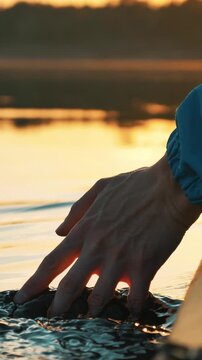 Man's hand touching the water's surface from a moving kayak during a beautiful golden hour, creating delicate ripples and splashes as the sunlight reflects on the calm lake water