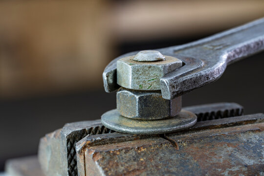 Macro of open end wrench turning rusty steel nut on bolt with washer clamped in heavy metal vice. Mechanics work, workshop repair, industrial tools and hardware concept