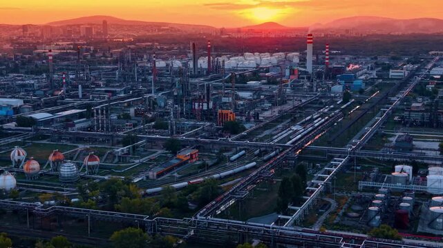 An intricate system of metallic pipes, structural steel framing, and processing machinery. Large industrial facility against beautiful orange sky at sunset.