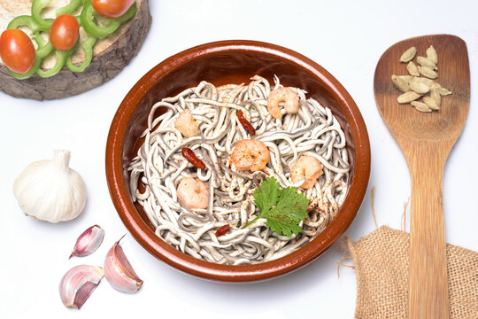 Traditional Spanish dish of gulas surimi baby eels cooked with garlic and prawns served in a classic brown clay ramekin on a white background