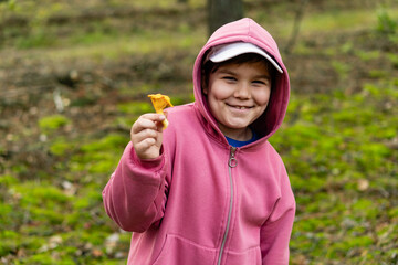 Naklejka premium Enthusiastic smiling little child with chanterelle mushroom in his hand. Focus on the boy. Boy showing edible mushroom he found in the forest. Weekend fun family activity.
