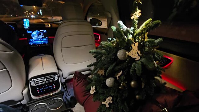 MOSCOW - JAN 7, 2026: Luxury car interior at night. Christmas tree in rear seat. Tree decorated with ornaments. Red ambient lighting . Modern dashboard and controls. Seat upholstery in neutral tone