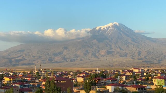 Mount Ararat rising in wide view above Dogubayazit at sunrise in eastern Turkey, showing snow covered summit, urban foreground, volcanic landscape, regional tourism, destination branding, and travel