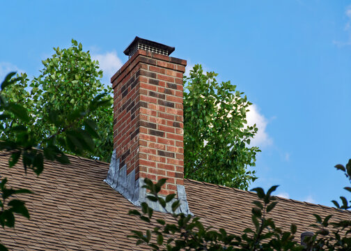 Red brick chimney with metal cap on an asphalt shingle roof in Boston
