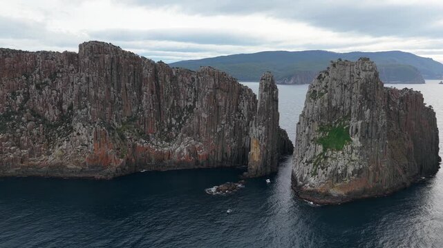 Aerial view of towering columnar rock cliffs beside a broad body of wa