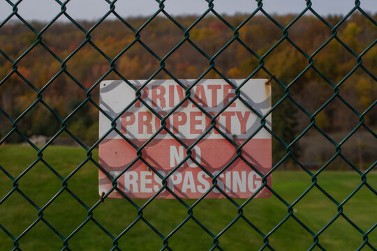 Private property no transposing sign on a fence, selective focus copy space background image, outdoors fall foliage in the background, authentic backdrop sign, warning keep out