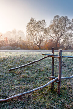 autumnal rural landscape in fog. countryside scenery with wooden fence in morning light. farm field by the road in hoarfrost