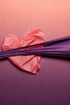 Pink paper heart wrapped with purple ribbon on pastel background