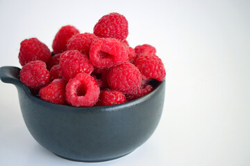 Raspberries in a black cup against a light background. Close-up of juicy, ripe berries. Food. Sweet berries harvested by farmers during the summer season. Organic. Vitamins. healthy raspberries. © Tatuss