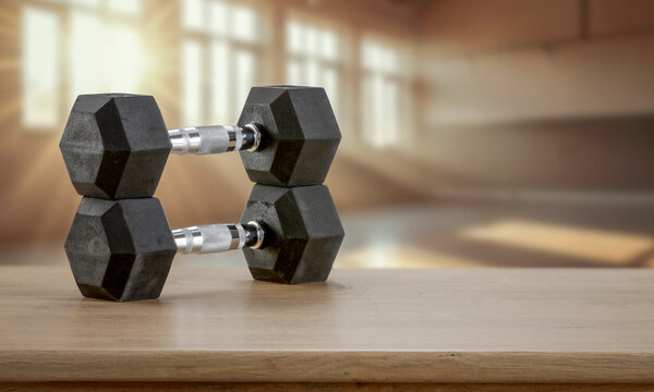 Dumbbells on wooden bench with blurred gym interior &ndash; fitness and strength training concept