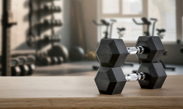 Dumbbells on wooden bench with blurred gym interior &ndash; fitness and strength training concept