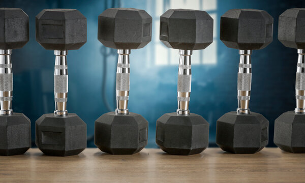 Dumbbells on wooden bench with blurred gym interior &ndash; fitness and strength training concept
