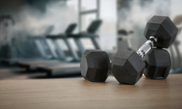 Dumbbells on wooden bench with blurred gym interior &ndash; fitness and strength training concept