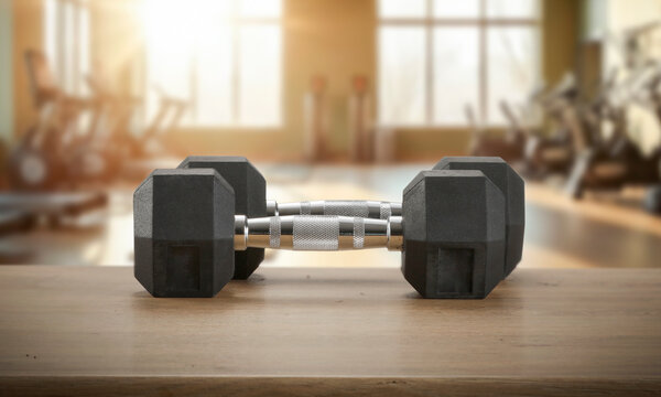 Dumbbells on wooden bench with blurred gym interior &ndash; fitness and strength training concept