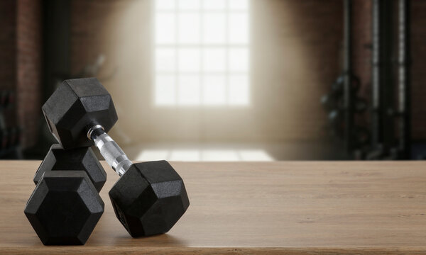 Dumbbells on wooden bench with blurred gym interior &ndash; fitness and strength training concept