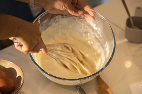 African American woman whisking batter in glass bowl with metal whisk on home kitchen counter