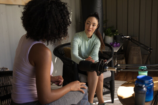 Diverse female friends recording in studio using microphones, mint top, shaker bottle nearby