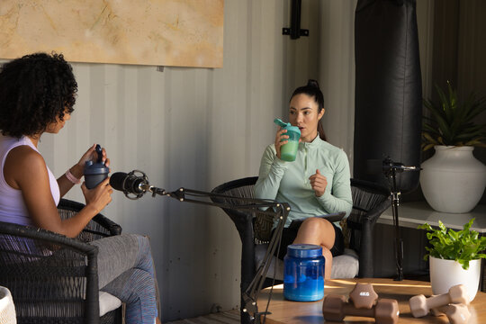 Diverse female cohosts in athletic wear recording fitness chat at studio with mics and 4KG weights