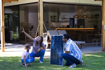 Fototapeta premium Family of three installing freestanding solar panel on lawn outside modern open-plan house