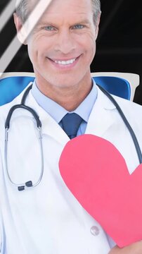 Animation of financial graphs, data and globe over happy caucasian doctor holding heart