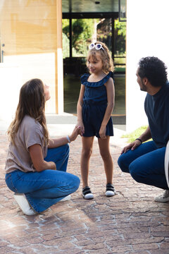 Family kneeling and crouching, holding child standing in navy romper at front door