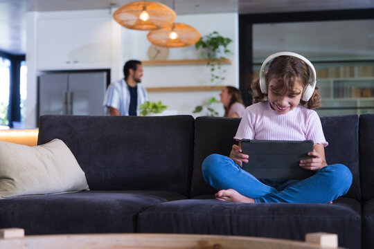 African American family, child on sofa using tablet with headphones parents chatting, copy space
