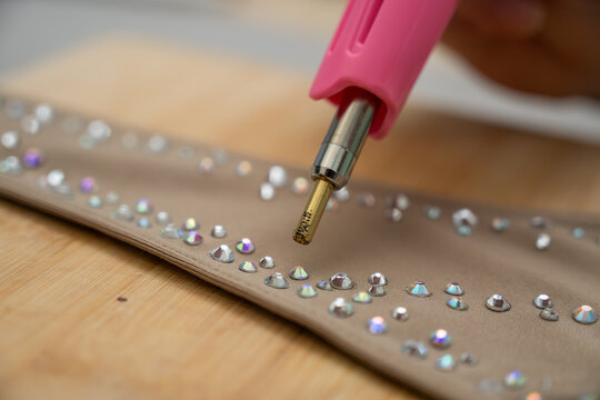 A woman glues rhinestones onto a gymnastics costume using a soldering iron. Hot fix.