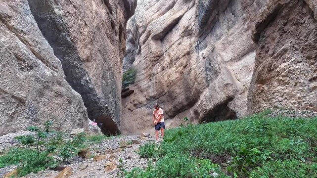 Woman exploring canyon in wide view among towering rock walls in Turkey, showing geological formations, green vegetation, hiking access, remote nature tourism, and rugged destination travel