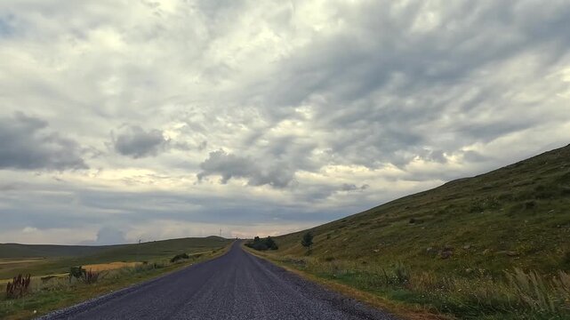 Vehicle traveling along empty highway, wide view, through rolling hills in Turkey under heavy clouds, showing road trip freedom, regional mobility, rural tourism, and self-drive travel concepts