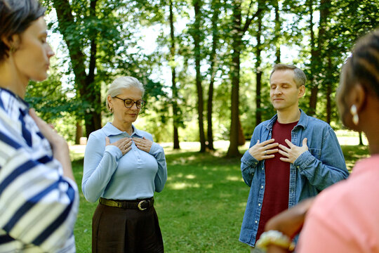 Diverse group of people practicing mindfulness and breathing exercises during outdoor therapy session in park, promoting mental health and wellness, medium shot