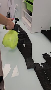Hand inflates lime-green helmet on table. Black straps lie nearby. White surface holds equipment. Person works with tools. Workshop setting visible. Objects arranged neatly electro muscle stimulation