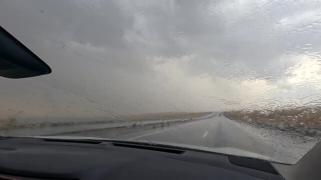 Car drives through heavy rain front view as windshield wipers clear water under dark storm clouds, showing hazardous road conditions, weather travel risk, vehicle safety, and severe storm driving